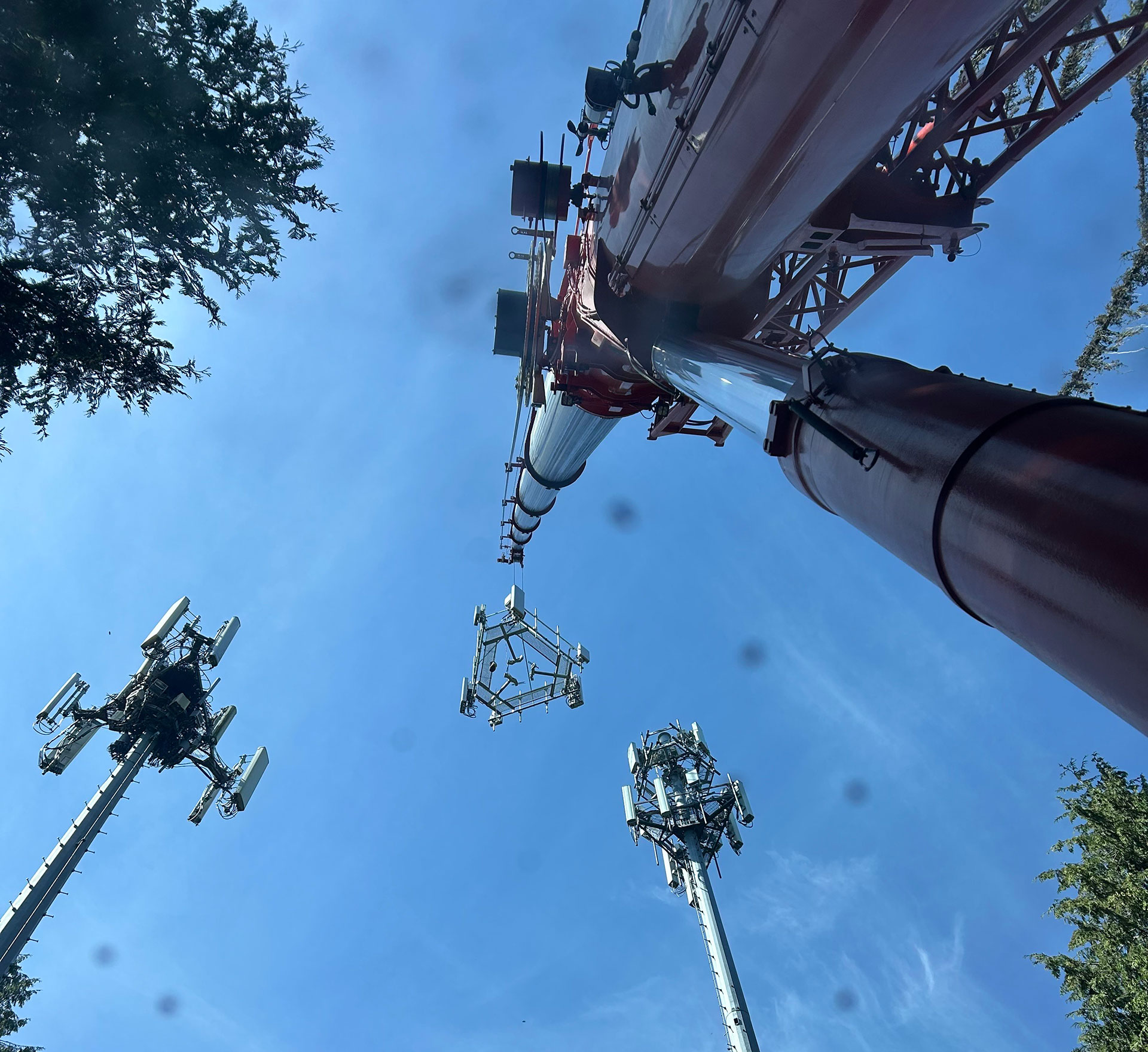 Image looking up a boom arm of a crane with two cell towers in the background | Crane Safe LLC