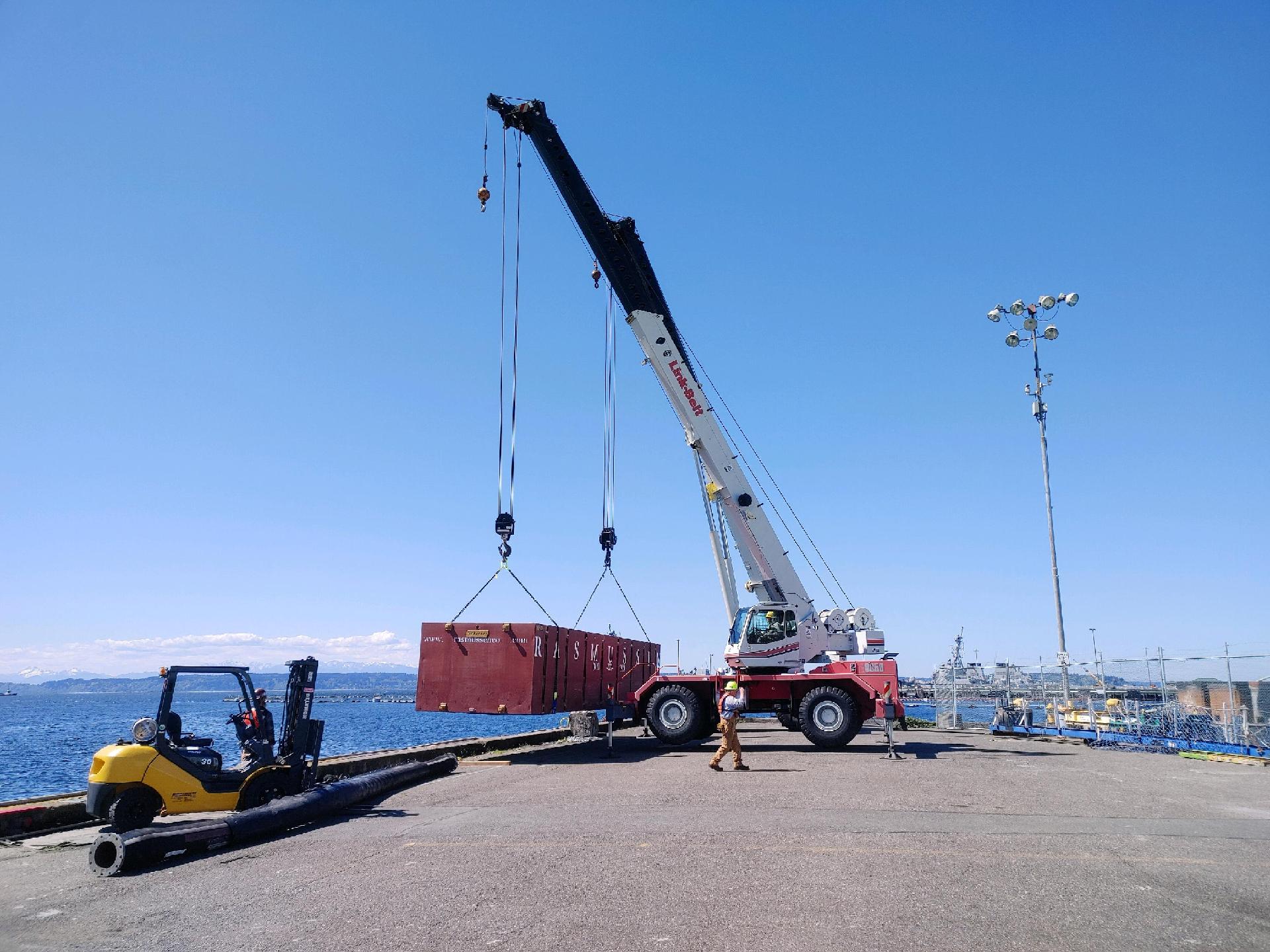 Image of a crane lifting a container onto a dock | Crane Safe LLC